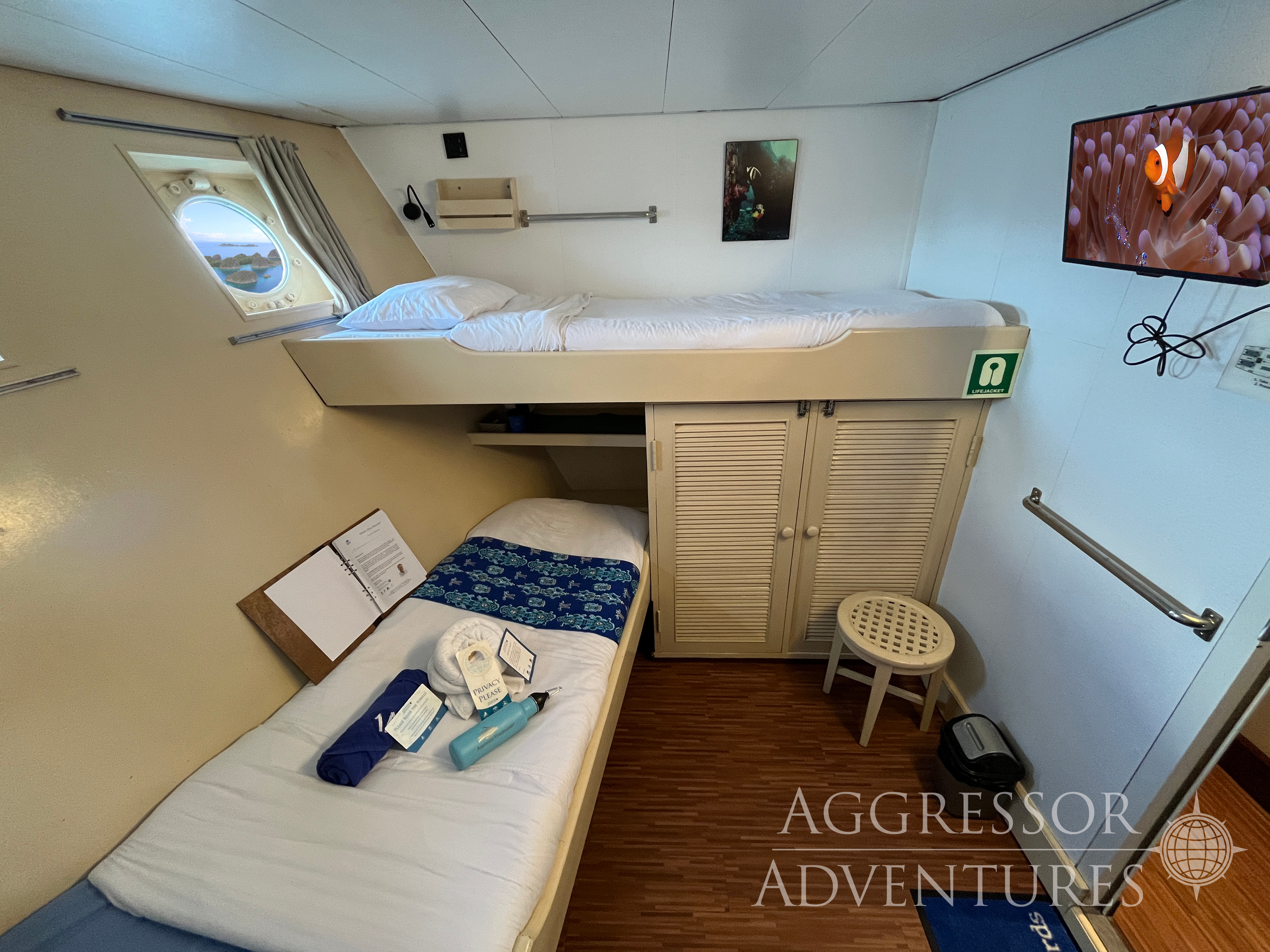 Comfortable deluxe twin stateroom with two single beds and porthole windows on Raja Ampat Aggressor